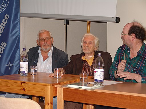 Drei weiße Männer an einem Tisch mit Wasser vor sich: Wolfgang Jeschke, Herbert W. Franke (ein Senior) und Erik Simon von der Seite 