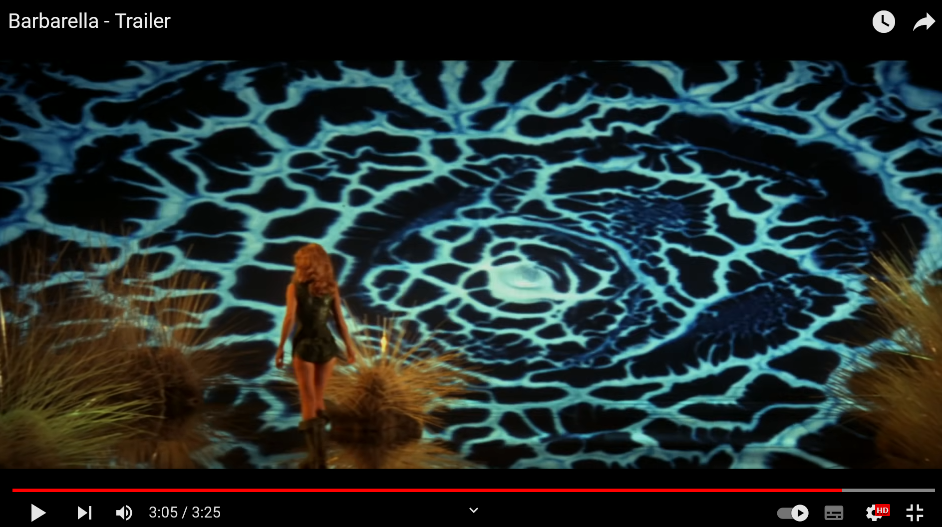 Ein Klick führt zum Trailer von Barbarella. Bild zeigt Barbarella, eine Frau mit vollen blonden Haaren und kurzer Lederkluft von hinten, wie sie durch eine Art Pilz-Spinnennetz-Landschaft läuft.