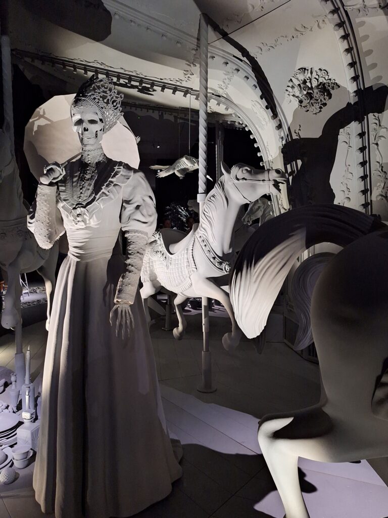 Schwarz-Weiß-Skulptur eines Karussells mit Pferden und einem Skelett in altertümlichem Kleid