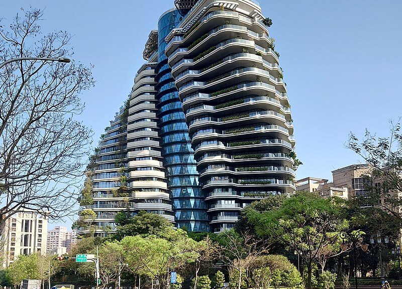 Ein scheinbar in sich vertretes Hochhaus an einer mit Bäumen bewachsenen Straße